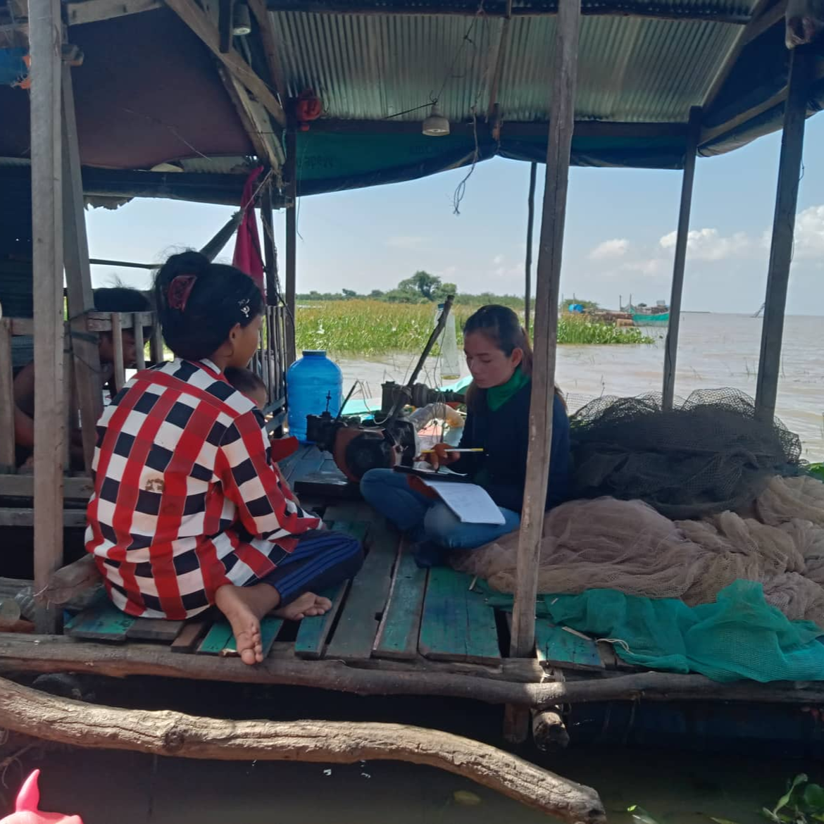 researcher collection data on a tablet with a local, sitting on a floating house